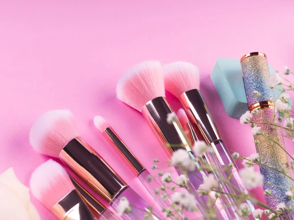 Brosses de maquillage tendance avec des produits sur fond rose avec des fleurs de gypsophila — Photo