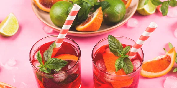 Освежающий летний красный коктейль в очках с кровью оранжевый и лайм на розовом фоне с мятой — стоковое фото