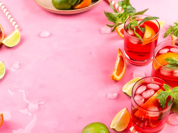 Δροσιστικό καλοκαιρινό κόκκινο κοκτέιλ σε ποτήρια με πορτοκάλι και λάιμ σε ροζ φόντο με μέντα — Φωτογραφία Αρχείου