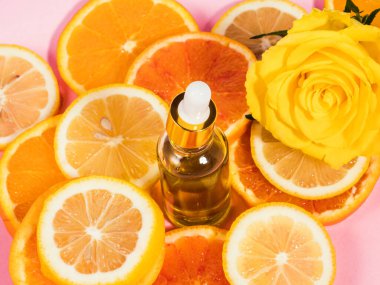 C vitamini serumu şişesi. Pembe arka planda damlatıcı ve turuncu narenciye dilimleri var.