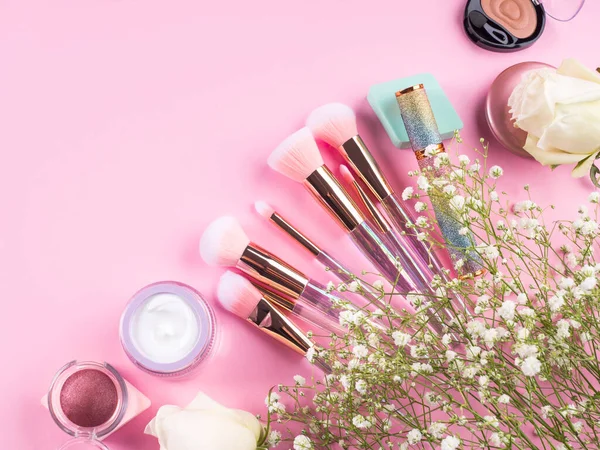 Brosses de maquillage tendance avec des produits sur fond rose avec des fleurs de gypsophila — Photo