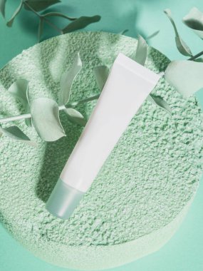 Tek renkli arka planda yeşil desenli podyum üzerine beyaz jenerik krem tüp