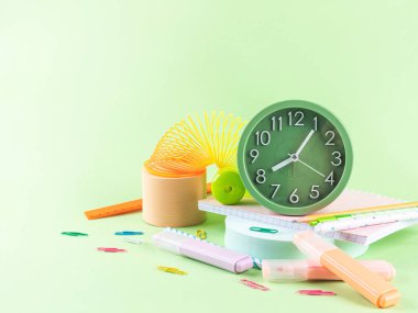 Okula dönmek, ofis malzemeleri konsepti. Alarm saati ile yeşil arkaplanda renkli kırtasiye