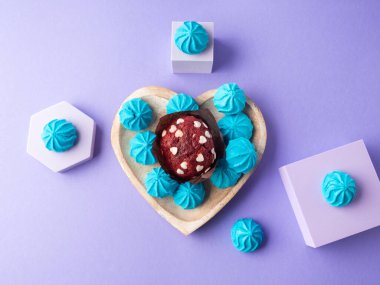 Heart shaped wooden dish with blue sweet meringues and red velvet muffin