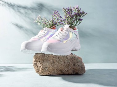 Taş podyumda turkuazda mor çiçekli beyaz spor ayakkabılar