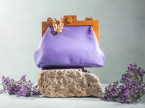 Natural áspero pódio de pedra cinza com bolsa feminina roxa e flores Imagens De Bancos De Imagens Sem Royalties