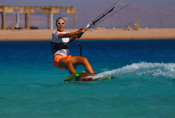 A young woman kite-surfer rides in greenish-blue sea under clear skies