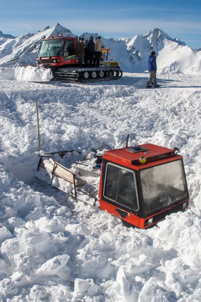 Um gato de neve está quase coberto de neve. Outro gato de neve está trazendo as pessoas para cima . — Fotografia de Stock