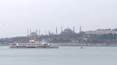 Ayasofya ve Sultanahmet arkada görünür ve feribot denizin üzerinde hareket ediyor.