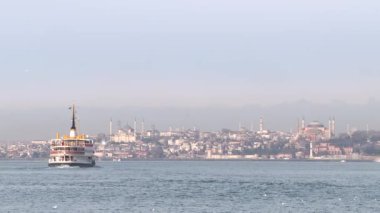Ayasofya ve Sultanahmet arkada görünür ve feribot denizin üzerinde hareket ediyor.
