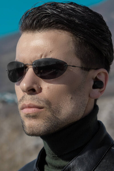 Portrait of a man with a smooth haircut and dark sunglasses looking like a secret agent or character from the movie The Matrix
