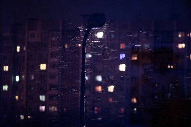 Geceleri pencereden manzara, apartmanların pencerelerinde ışık, yanan bir fener, ıslak kar.