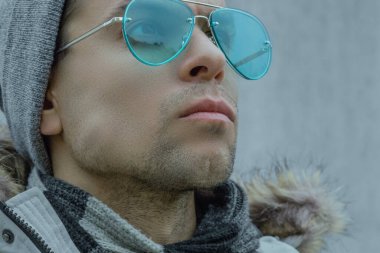 Turkuaz güneş gözlüklü ve kışlık ceketli bir adamın yakın plan portresi.