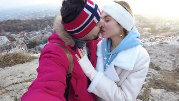 Un mec et une fille se tiennent debout sur le bord d'un rocher dans une étreinte en hiver et embrassent, la joie apparaît sur leurs visages — Video