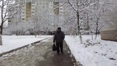 Yaşlı bir adam elinde bir paketle kış mevsiminde kaldırımda yürür.