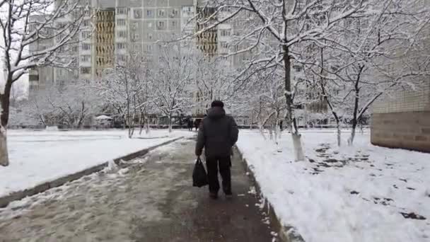 Un homme âgé marche avec un paquet dans les mains sur le trottoir, en hiver — Video