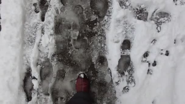 Un hombre con pantalones y botas calientes camina ordenadamente a lo largo de la acera en la que la nieve húmeda se ha congelado y formado hielo. — Vídeos de Stock