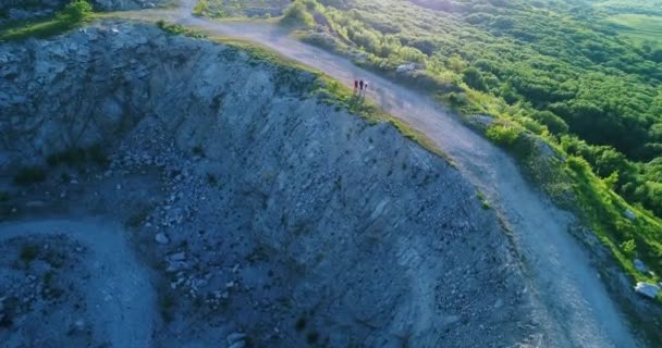 渓谷の上を飛行するドローンは、観光客が日没の晴れた夏の日に狭い岩に沿って歩く — ストック動画