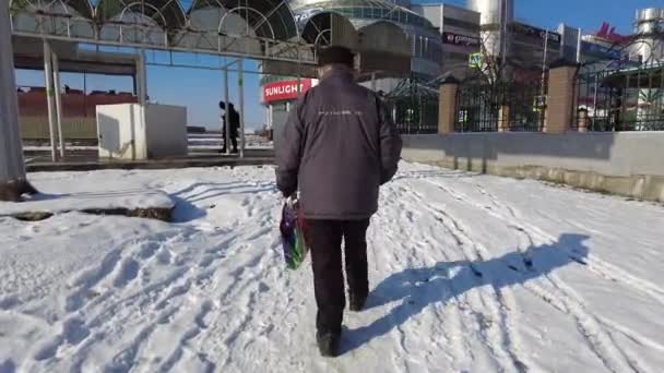 Mineralnye Vody, Stavropol Terület, Oroszország 01.10.2021 Egy idős ember egy csomaggal a kezében sétál egy élelmiszerboltba, amely arra készül, hogy átkeljen egy széles utcán, közel egy bevásárlóközponthoz — Stock videók