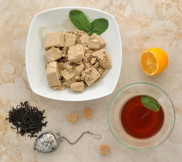 Oriental sweets - halva in a plate with mint leaves. black tea i — Stock Photo, Image