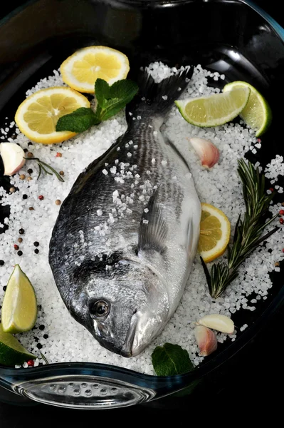 Dorado poisson est dans un plat en verre avec du sel, romarin, ail, citron vert a — Photo