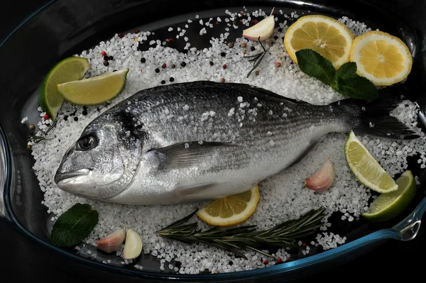 Dorado poisson est dans un plat en verre avec du sel, romarin, ail, citron vert a — Photo