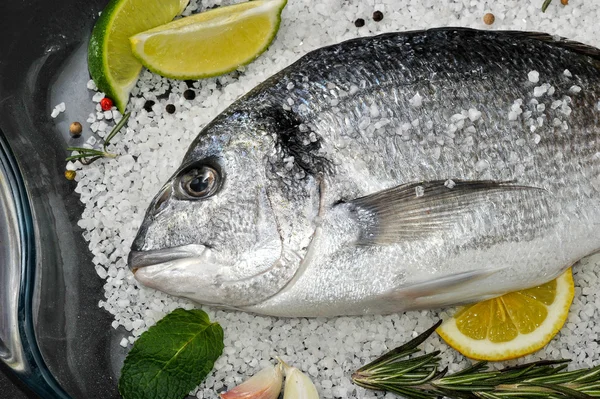 Dorado pescado está en plato de vidrio con sal, romero, ajo, lima a — Foto de Stock