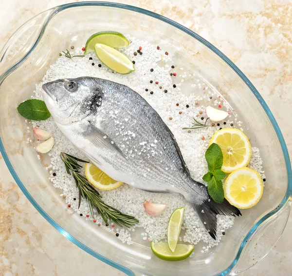 Dorado pescado está en plato de vidrio con sal, romero, ajo, lima a — Foto de Stock