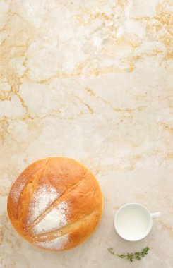 white round bread with a mug of milk on a marble background.