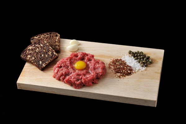 Carne picada con huevo crudo sobre un tablero de madera sobre fondo negro — Foto de Stock