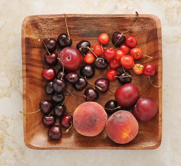 Фруктова тарілка - персики, сливи, вишні на дерев'яній тарілці . — стокове фото