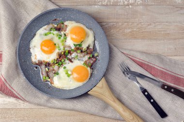 Kızarmış yumurta, domuz pastırması ve tavada yeşil soğan.