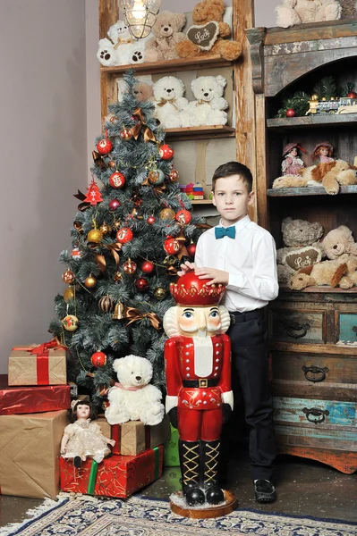 Christmas boy and the Nutcracker around Christmas tree with gift — Stock Photo, Image