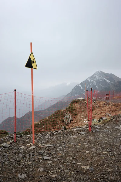 Sign danger of falling from a height on top of the mountain rose — Stock Photo, Image