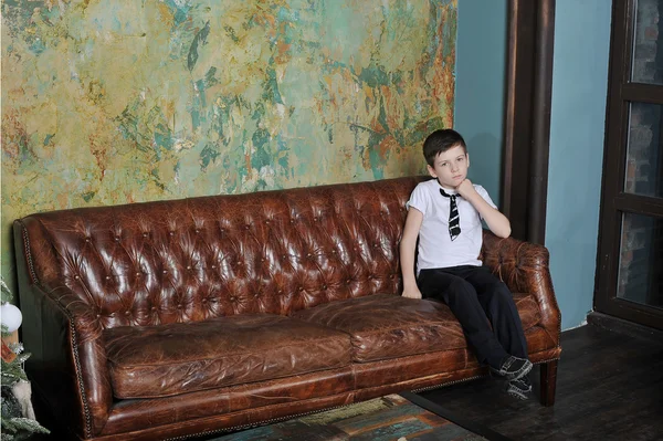 Niño sentado en un sofá de cuero — Foto de Stock