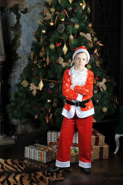 Lille dreng i kostume af julemanden stående omkring jul t - Stock-foto