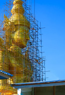 Tayland, Nakhon Pathom 'da mavi gökyüzüne karşı inşaat halindeki iskelenin alçak açısı ve büyük altın Buda heykeli.