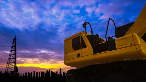 Part of yellow excavator with pile driver and many precast concrete piles in construction site against colorful sunset sky background