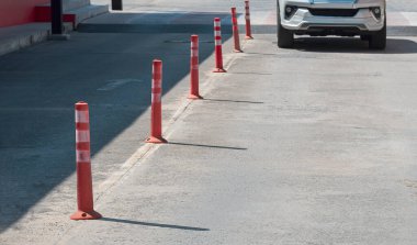 Turuncu plastik trafik direklerinden oluşan sıra. Bulanık hareketli beyaz arabanın ön görüntüsü. Açık otoparka doğru yavaşça gidiyor.