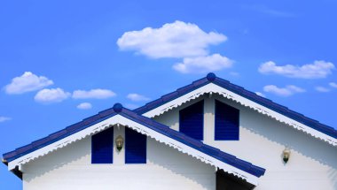 Mavi lifli çimento kiremit çatısının ön görüntüsü beyaz ahşap evin üzerine damlayan bir damlacıkla beyaz bulutlar ve mavi gökyüzü arka planı