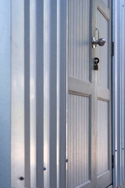 Kapı tokmağındaki seçici odak, perspektif yan görünümü ve dikey çerçevesi olan kıvrımlı metal duvardaki gri kapılı asma kilit.