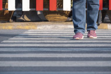 Front view of human legs walking across the street on zebra crossing in public area