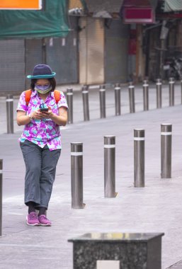 Asyalı bayan turist, sokakta dikey çerçevede yürürken metal bariyerler arasında dururken akıllı telefon kullanıyor.