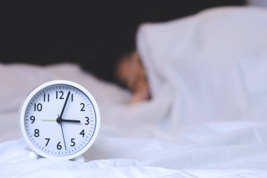 Saat 3 yönündeki beyaz çalar saate odaklan. Kadının arka planı bulanık. Geceleri yatakta uyuyor.