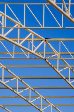 İnşaat alanındaki metal bina çatı yapısının dikey çerçevedeki mavi gökyüzü arka planına göre düşük açılı görüntüsü