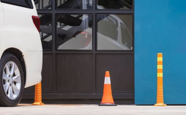 Turuncu trafik konileri ve modern restoranın cam duvarının yanındaki park alanında beyaz araba parkı olan plastik direkler.