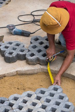 Kamu parkındaki kaldırım kaldırım çalışmasında kesilen çim taşı bloğunun kaldırım boşluklarını ölçmek için mezura kullanan inşaat işçisinin yüksek açılı görüntüsü 