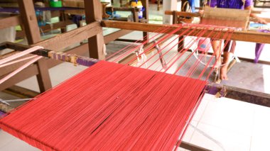 Close-up of traditional handloom weaving with bright red threads, showcasing Thai textile craftsmanship, handmade silk production, and local artisan culture in Thailand