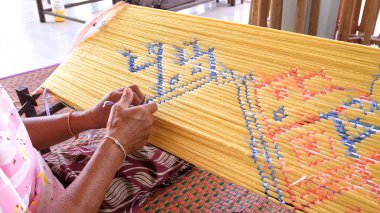 Traditional Thai hand weaving process with colorful silk threads, showing artisan craftsmanship and intricate textile patterns in local handmade fabric production.