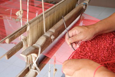 Geleneksel ahşap dokuma tezgahına iğneyle kırmızı ipek kumaş desenleri ören el dokuma, Tayland 'da yerel işçiliği, kültür mirasını ve el yapımı tekstil sanatını gösteren.